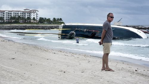 Yacht owner Thomas Baker stands on the beach as the salvage company employees work on towing his yacht ashore earlier this month. (Melanie Bell / Daily News)