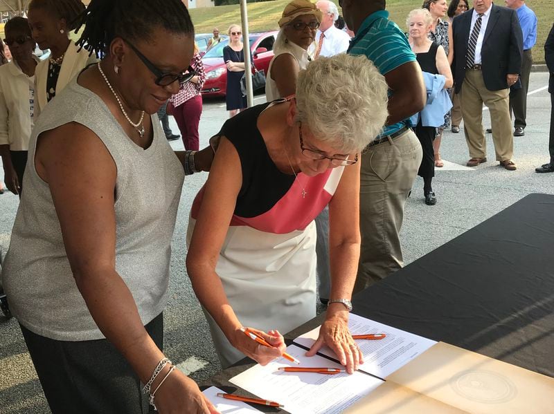 Lawrenceville Mayor Judy Jordan Johnson, right, signs a resolution saving the historic Hooper Renwick School on Thursday while Theresa Bailey, a graduate of the school and chairperson of the Hooper Renwick Legacy Preservation Committee, looks on.