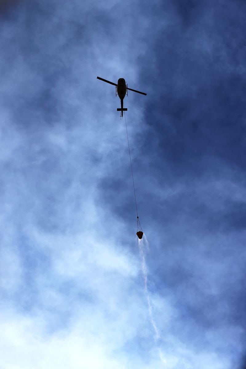 A Bell 205 tac 2 helicopter is surrounded by smoke while flying a bucket of water to fight the Rock Mountain Fire on Monday, Nov. 21, 2016, in Clayton.