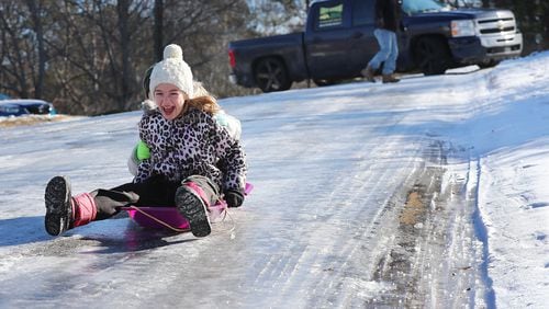 Kaylee Collins (front) and her friend Lana Anderson, both 9, sled down ice covered Pine Terrace Road away from a abandoned truck stuck on the ice in Cherokee Falls Estates at the Lake subdivision in the aftermath of the winter storm on Sunday, Jan. 8, 2017, in Canton.