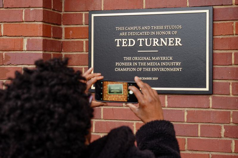 A woman takes a photo of a plaque on  an AT&T WarnerMedia building dedicating  it to Ted Turner, the founder of Turner Broadcasting System, on Friday, December 6, 2019, in Atlanta. (Elijah Nouvelage/Special to the Atlanta Journal-Constitution)