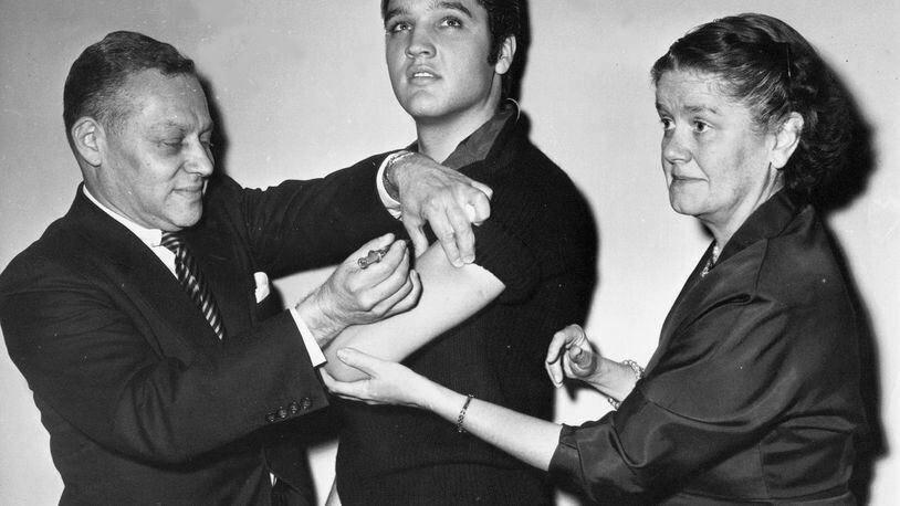 FILE - In this Oct. 28, 1956 file photo, Elvis Presley receives a Salk polio vaccine shot in New York City from Dr. Harold Fuerst, left. At right is Dr. Leona Baumgartner, commissioner of the New York City health department. Tens of millions of today's older Americans lived through the polio epidemic, their childhood summers dominated by concern about the virus. Some parents banned their kids from public swimming pools and neighborhood playgrounds and avoided large gatherings. Some of those from the polio era are sharing their memories with today's youngsters as a lesson of hope for the battle against COVID-19. Soon after polio vaccines became widely available, U.S. cases and death tolls plummeted to hundreds a year, then dozens in the 1960s, and to U.S. eradication in 1979.(AP Photo/File)