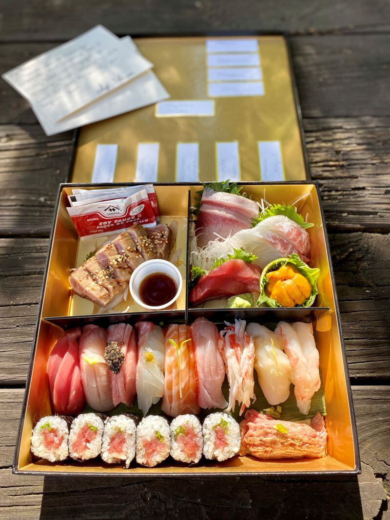 The $70 omakase bento box from Yakitori Jinbei comes in a black box tied with a ribbon and includes a thank-you note from the chef. Labels on the underside of the lid identify the contents. (Wendell Brock for The Atlanta Journal-Constitution)