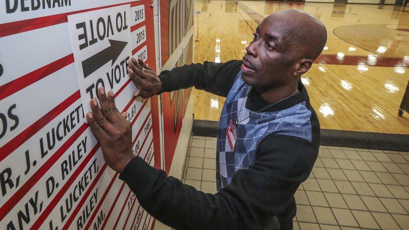 Poll worker Harold Miller posts vote signs throughout the gym at Henry W. Grady High School on Tuesday Dec. 4, 2018. JOHN SPINK/JSPINK@AJC.COM