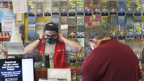 A clerk adjusts his protective mask while waiting on a masked customer at Ted's Stateline Mobil on Wednesday, June 24, 2020 in Methuen, Mass.