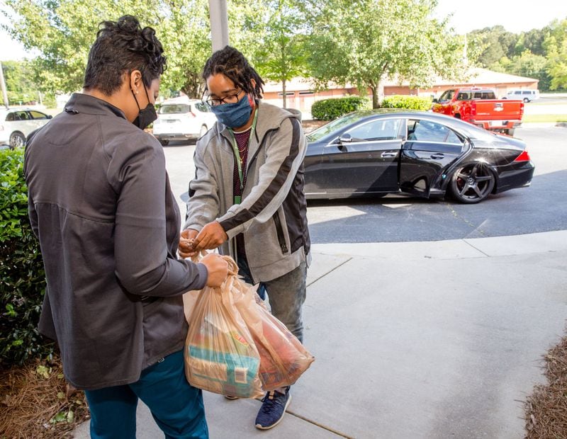 Kyesha Walker, left, who is a clinical supervisor for DeKalb Medical, takes her groceries from Kyle Ford, an Instacart delivery gig worker. Walker feels that she is being more responsible by having groceries delivered since she is working in the medical field. (Jenni Girtman for Atlanta Journal-Constitution)
