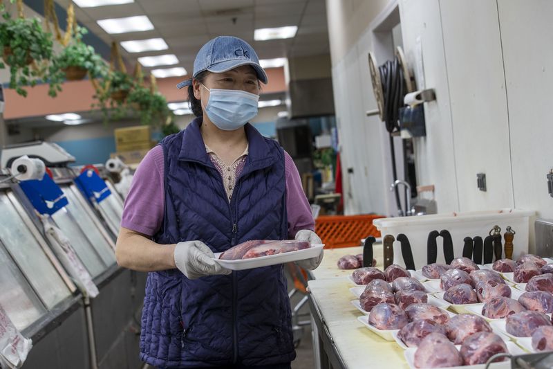 Yan Ning, an employee at the Dinho Supermarket of Atlanta, wears a mask and gloves while wrapping pairs of beef shanks to sell in the meat department at the grocery store located inside the Atlanta Chinatown Shopping Mall in Chamblee, Friday, July 31, 2020. (ALYSSA POINTER / ALYSSA.POINTER@AJC.COM)
