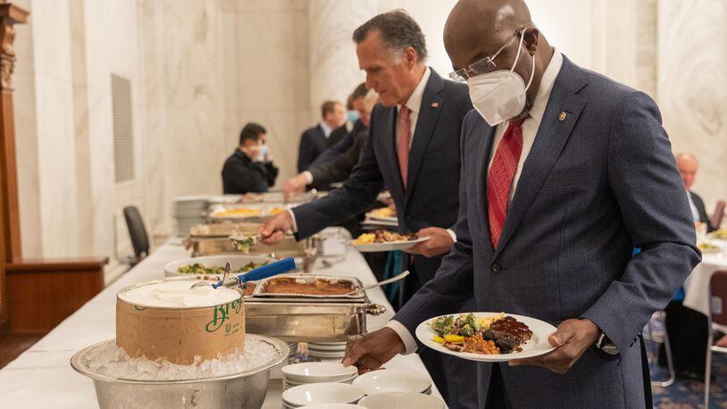 Democratic U.S. Sen. Raphael Warnock of Georgia and Republican U.S. Sen. Mitt Romney of Utah fill their plates during a bipartisan barbecue luncheon Thursday on Capitol Hill in Washington. Warnock helped relaunch the annual gathering of the two parties, which then-U.S. Sen. Johnny Isakson of Georgia started 13 years ago.