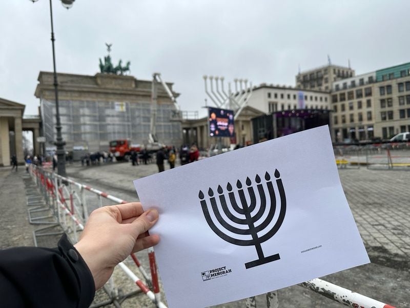 An ally stands at at the Brandenburg Gate in Berlin holding up a print-out of a menorah downloaded from the Project Menorah website. Courtesy: Project Menorah
