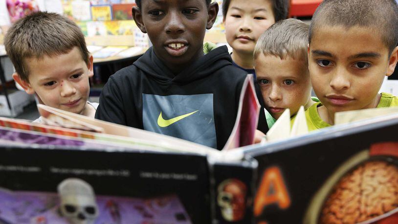 Fourth graders at a book fair at their school media center are fascinated by a science book.