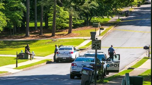 A witness (seated left) talks with Gwinnett County police after a shooting on Highland Gate Circle on Monday morning. According to police, a woman opened fire on a school bus as it was leaving a bus stop.