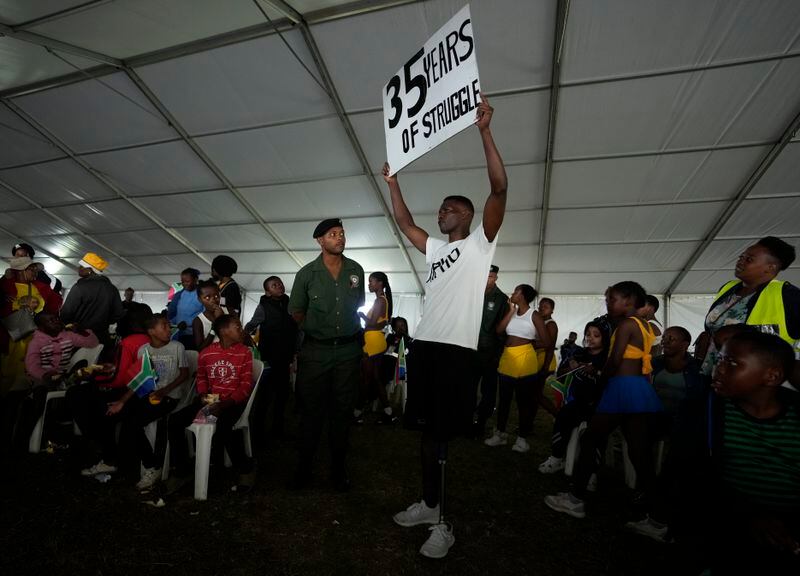A protester holds up a poster as he attends Freedom Day celebrations in Pretoria, South Africa, Saturday April 27, 2024. The day marks April 27 when the country held pivotal first democratic election in 1994 that announced the official end of the racial segregation and oppression of apartheid. (AP Photo/Themba Hadebe)