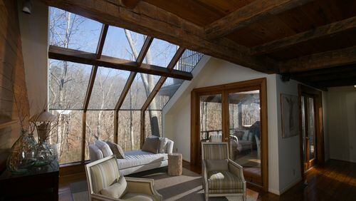 The Landers' living room is shown with a wall of windows in the background overlooking the woods. The ceiling above the living room is reclaimed wood from a railroad depot in North Carolina.  PHOTO / JASON GETZ
