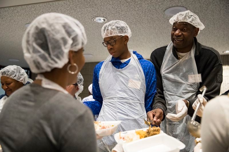 Former Atlanta Hawks player Dikembe Mutombo (right) and his son, Ryan (left), serve meals during the annual Hosea Helps Thanksgiving dinner Thursday, Nov. 23, 2017, at the Georgia World Congress Center in Atlanta. (Alyssa Pointer / Alyssa.Pointer@ajc.com)