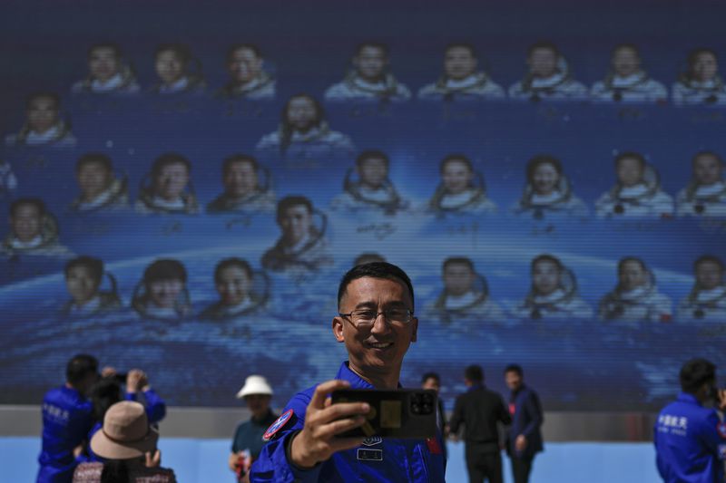 A staff member takes a selfie with a billboard depicting Chinese astronauts on the past Shenzhou missions after Chinese astronauts for the upcoming Shenzhou-18 mission met with media members at the Jiuquan Satellite Launch Center in northwest China, Wednesday, April 24, 2024. (AP Photo/Andy Wong)