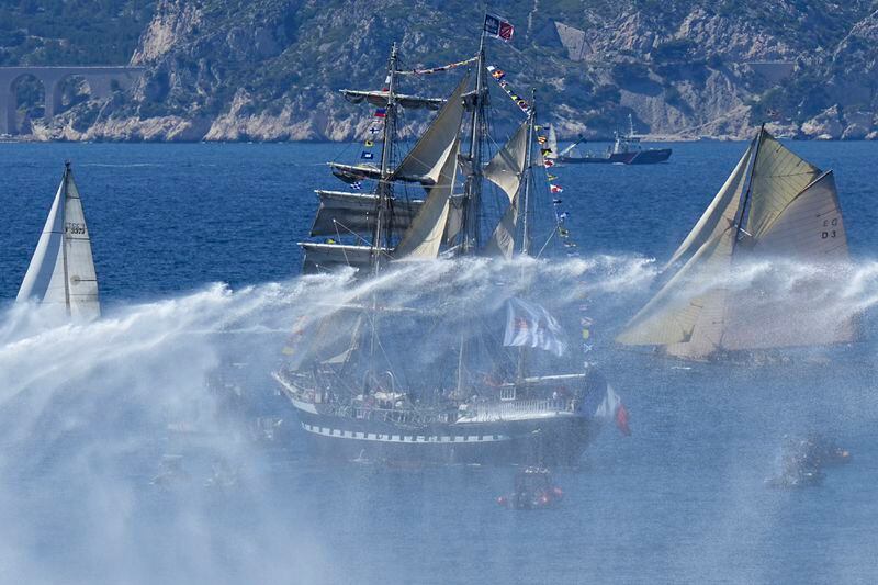 The Belem, the three-masted sailing ship bringing the Olympic flame from Greece, is escorted by other boats while a tugboat sprays water in the foreground, when approaching Marseille, southern France, Wednesday, May 8, 2024. After leaving Marseille, a vast relay route is undertaken before the torch odyssey ends on July 27 in Paris. The Paris 2024 Olympic Games will run from July 26 to Aug.11, 2024. (AP Photo/Laurent Cipriani)