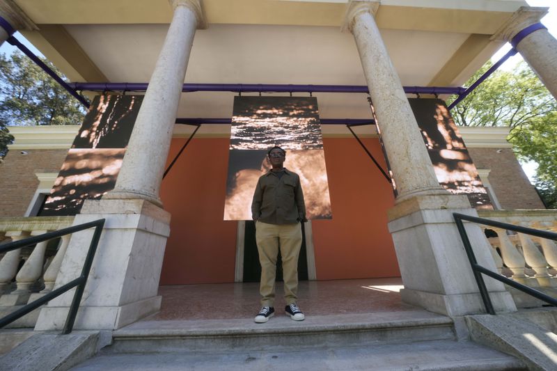 British artist John Akomfrah poses in front of the British pavilion at the 60th Biennale of Arts exhibition in Venice, Italy, Tuesday, April 16, 2024. The Venice Biennale contemporary art exhibition opens Saturday for its six-month run through Nov. 26. The main show titled 'Stranieri Ovunque – Foreigners Everywhere' is curated for the first time by a Latin American, Brazilian Adrian Pedrosa. Pedrosa is putting a focus on underrepresented artists from the global south, along with gay and Indigenous artists. Alongside the main exhibition, 88 national pavilions fan out from the traditional venue in Venice's Giardini, to the Arsenale and other locations scattered throughout the lagoon city. (AP Photo/Luca Bruno)
