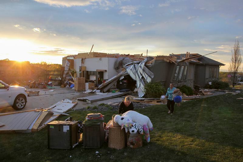 Two woman help carry a friend's belongings out of their damaged home after a tornado passed through the area in Bennington, Neb., Friday, April 26, 2024. (AP Photo/Josh Funk)