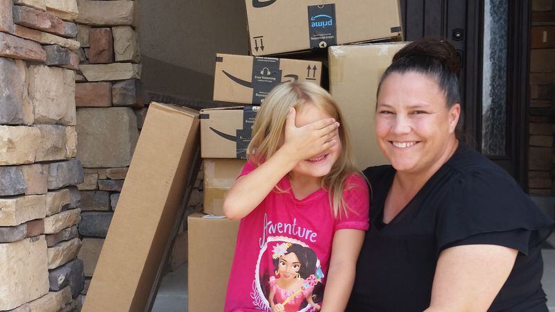 Catherine Lunt and her daughter, 6-year-old Katelyn, pose with a stack of Amazon boxes full of toys Katelyn ordered without her mom's permission.