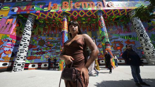 Brazilian artist Manauara Clandestina poses in front of the main entrance of the main pavilion at the 60th Biennale of Arts exhibition in Venice, Italy, Tuesday, April 16, 2024. The Venice Biennale contemporary art exhibition opens Saturday for its six-month run through Nov. 26. The main show titled 'Stranieri Ovunque – Foreigners Everywhere' is curated for the first time by a Latin American, Brazilian Adrian Pedrosa. Pedrosa is putting a focus on underrepresented artists from the global south, along with gay and Indigenous artists. Alongside the main exhibition, 88 national pavilions fan out from the traditional venue in Venice's Giardini, to the Arsenale and other locations scattered throughout the lagoon city. (AP Photo/Luca Bruno)