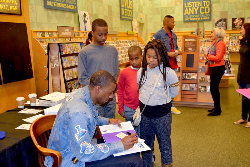 (From left) Will, Preston and Gabby Flournoy watch as NFL player Malcolm Mitchell signs their copies of his book, “The Magician’s Hat.” (Alexis Stevens/astevens@ajc.com)