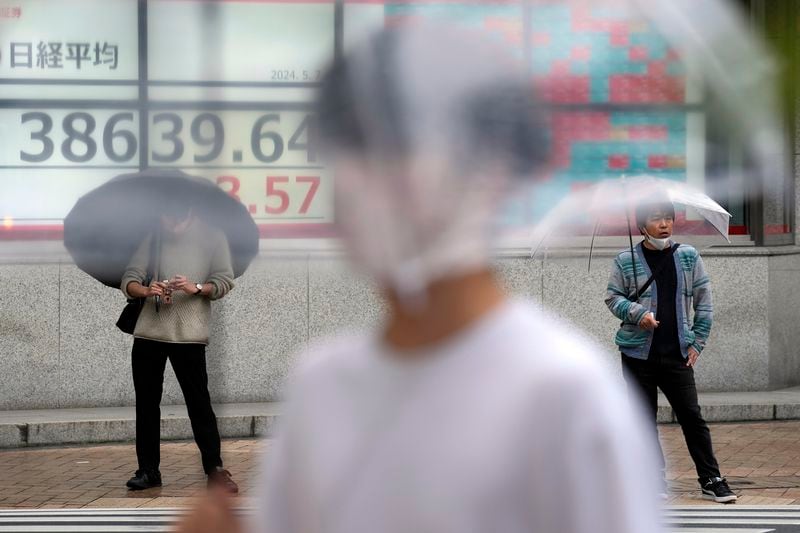 People stand in the rain near an electronic stock board showing Japan's Nikkei 225 index at a securities firm Tuesday, May 7, 2024, in Tokyo. (AP Photo/Eugene Hoshiko)