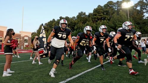 GAC players from left to right; Addison Nichols (72), Gannon Hearts (20), Luke Hicks (7), and Bobby Kincade (77) run onto the field before their game against Lovett at Greater Atlanta Christian Friday, Sept. 11, 2020 in Norcross. (Jason Getz/For the AJC)