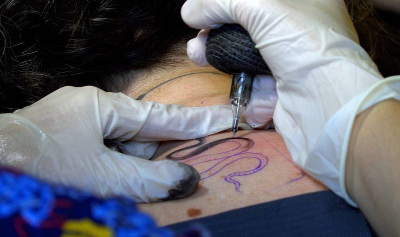 Van Bixler, a tattoo artist at Smoking Mirror Tattoo Gallery in Columbus, Georgia, adds a tattoo of a small snake to Ledger-Enquirer reporter Sundi Rose’s upper back. (Photo Courtesy of Mike Haskey)