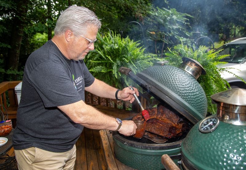 Hal Boyd bastes three pork butts on his Big Green Egg to make pulled pork sandwiches for healthcare workers at Piedmont Hospital at his North Druid Hills Home. He and his friends have made and delivered more than 4,000 BBQ sandwiches to area hospitals and other first responders since the pandemic began. PHIL SKINNER FOR THE ATLANTA JOURNAL-CONSTITUTION.