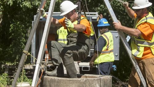 Workers pulled a crew member through a manhole after lowering him into DeKalb County’s sewer system to inspect sediment build-up. Chad Rhym/ Chad.Rhym@AJC.com