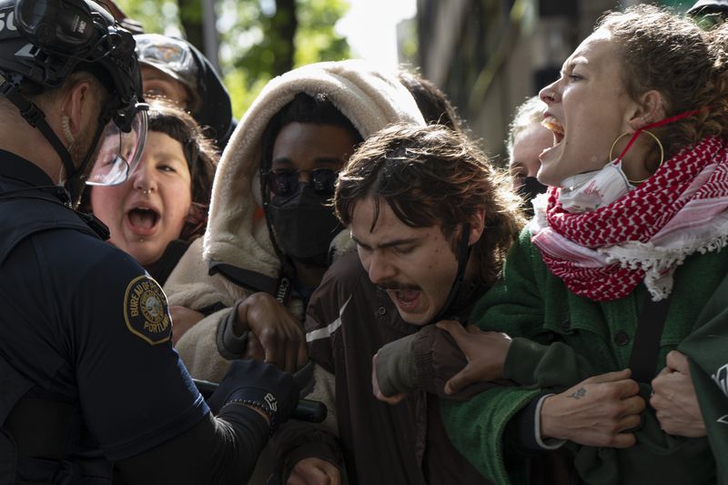 A group of pro-Palestinian protesters try to block a van carrying people detained by Portland police on Thursday, May 2, 2024, in Portland, Ore. Portland police cleared out a library on campus that protesters had occupied since Monday. Officers said they made 22 arrests Thursday. (AP Photo/Jenny Kane)