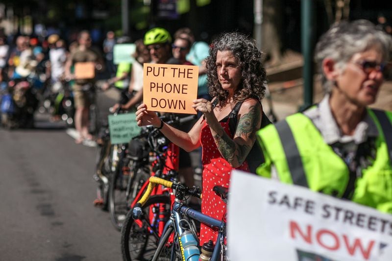 Kat Jones holds a sign during a rally on West Peachtree Street near 15th Street on Wednesday, July 24, 2019, in Atlanta. Organizers joined together as a “human protected sidewalk, bike and scooter lane” demanding the city prioritize protected bike and scooter lanes. BRANDEN CAMP/SPECIAL