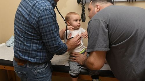 Dr. Greg McHan (left) examines Lenny Falletta III, 18 months, (center) of Blairsville, Georgia, with a little help from Lenny Falletta Jr. (right) at the Georgia Mountains Health clinic in Blue Ridge, Ga. on September 28 2017. Steve Miracle runs Georgia Mountains Health, which provides healthcare at seven location including two in Blue Ridge, and half of their patients have no insurance whatsoever. (PHOTO by Rebecca Breyer)