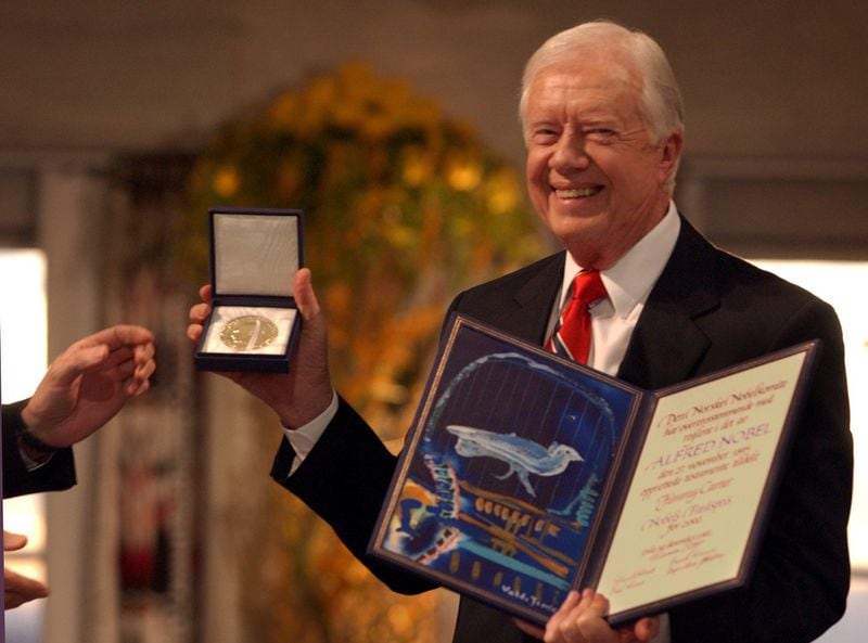 Nobel Peace Prize winner Jimmy Carter shows the Nobel medal and diploma to the audience after the presentation from Gunnar Berge (hands pictured)(Chairman of the Norwegian Nobel Committee) in the Oslo City Hall, December 10, 2002. (JOEY IVANSCO/staff photo).