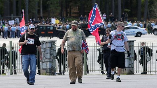 Joseph Andrews, from left, of Woodstock, Shaun Winkler of Mississippi and James Berry of Michigan walk through a designated protest area in support of the Confederate battle flag, as hundreds of counter-protesters can be seen 100 yards behind them at Stone Mountain Park on a Saturday afternoon in April. Ben Gray,bgray@ajc.com