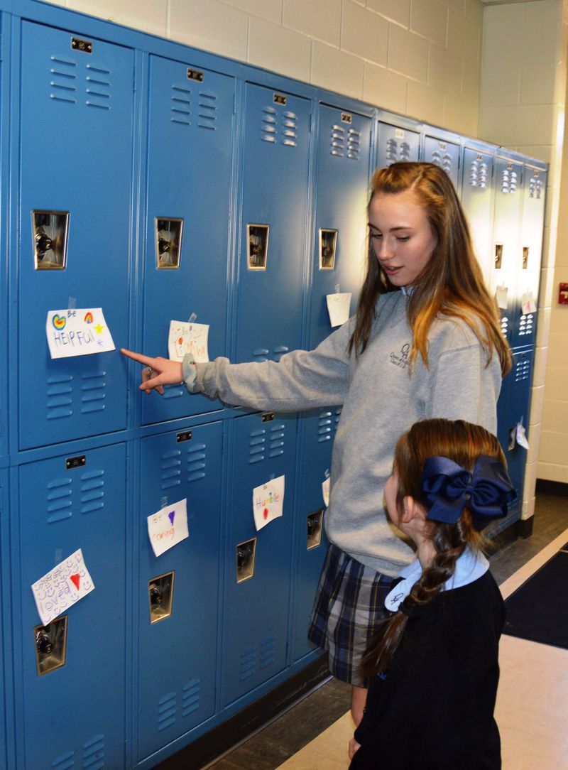 Hayden Parkinson shows Caitlin Davis words of encouragement that her first-grade class taped to lockers at Queen of Angels Catholic School. Instead of walking out of school to protest gun violence, Davis, along with fellow eighth-graders Maddy Muir and Mark Ruppenthal, decided to use the 17 minutes to talk about how they could curtail the violence by being kinder to one another. CONTRIBUTED