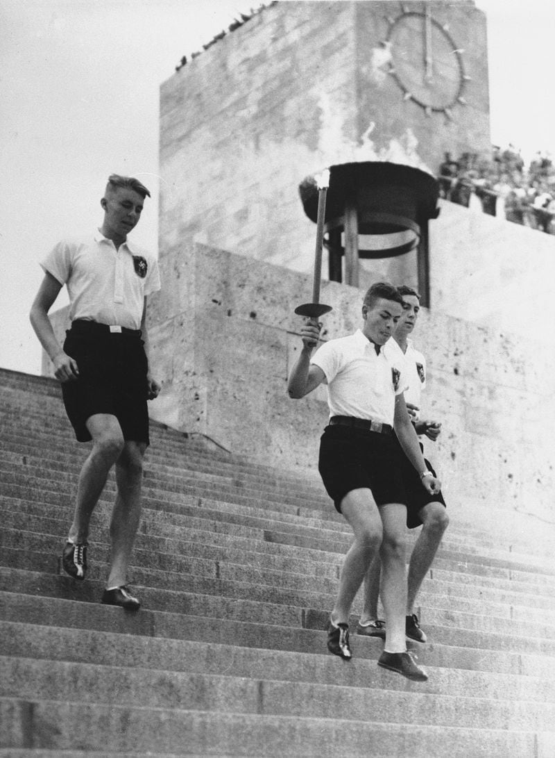 FILE - The Olympic flame is carried by a torch bearer from the Olympiastadion in Berlin en route to the stadium in Gruenau, Germany for the opening of the Olympic Rowing and Canoeing events on the Regatta course, Aug. 1, 1936. On Tuesday, April 16, 2024 the flame for this summer's Paris Olympics will be lit and be carried through Greece for more than 5,000 kilometers (3,100 miles) before being handed over to French organizers at the Athens site of the first modern Olympics. (AP Photo, File)