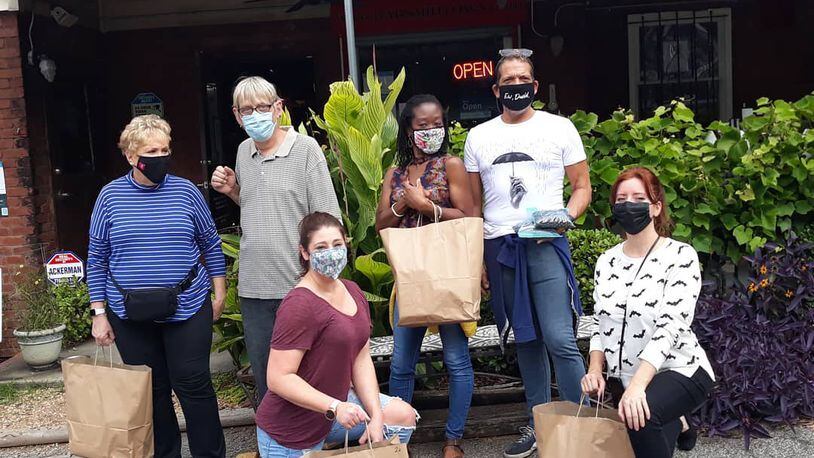 Six people wearing face masks pose holding paper bags in front of Babs restaurant.