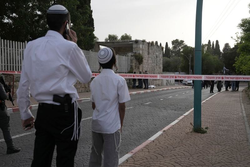 An armed Israeli man and child watch police investigate the scene of a stabbing as the body of a suspected attacker lies covered in Ramle, central Israel, Friday, April 26, 2024. The attack, which Israel's rescue services said was carried out by a militant, injured an 18-year-old woman. (AP Photo/Mahmoud Illean)