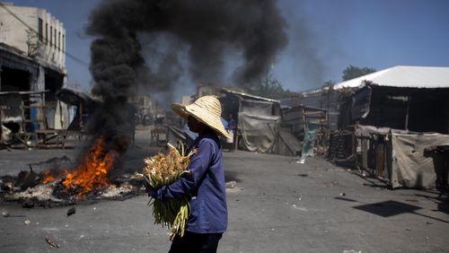 A street vendor walks past burning tires set up by anti-government protesters during a general strike in Port-au-Prince, Haiti, Monday, July 9, 2018. A nationwide, general strike and protest was called to demand the resignation of Haiti's President after his government agreed to reduce subsidies for fuel. The fuel hike was suspended after widespread, violent protests broke out on Friday and over the weekend.
