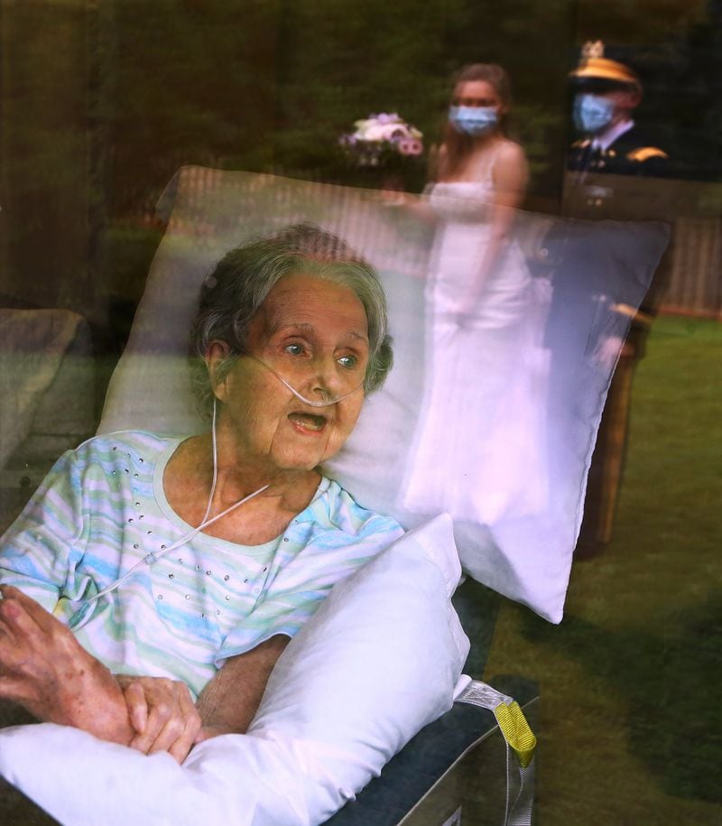 Jacqueline Cavender, 84, reacts as her grandson U.S. Army second lieutenant Robert Costea and his bride Sarah recreate their wedding for her during a window visit in June at Westbury Medical Care & Rehab. The couple, who married on May 30th, traveled from North Carolina to fill Cavender with joy and introduce the bride. CURTIS COMPTON / CCOMPTON@AJC.COM