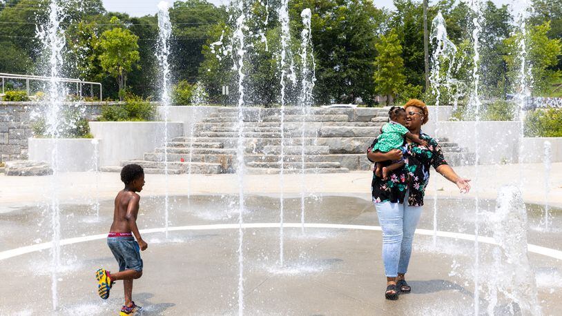 Tri Hall, 7, runs as his mother Tyii and sister Vee, 9 months, play in the splash pad at Rodney Cook Sr. Park in the Vine City neighborhood of Atlanta on Tuesday, July 18, 2023. (Arvin Temkar / arvin.temkar@ajc.com)