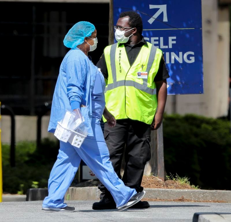 A medical worker (left) and traffic control employee both wear masks on the campus of Emory University Hospital Midtown on Friday. JOHN SPINK/JSPINK@AJC.COM