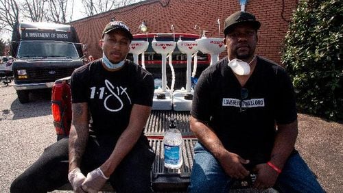 Hip hop recording artist Lecrae, left, and Love Beyond Walls founder Terence Lester, right, sit on a truck bed filled with portable wash stations on Thursday, March 19, 2020 in College Park, Georgia. The wash stations were distributed by Lecrae and volunteers with Love Beyond Walls, a non-profit, throughout Atlanta in areas with a high density of homeless persons. (AP Photo/ Ron Harris)