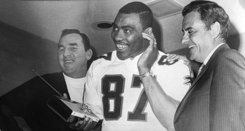 Falcons owner Rankin Smith (right) and coach Norb Hecker (left) join defensive end Claude Humphrey in listening to the news that he was drafted over the radio. AJC file