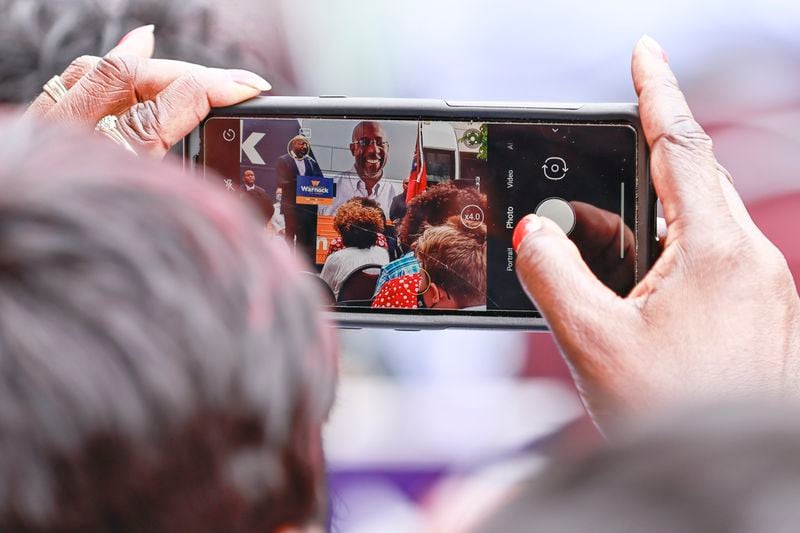 A woman takes a photo of Democratic U.S. Sen. Raphael Warnock as he speaks to the crowd Thursday during a campaign rally in Milledgeville. (Natrice Miller/natrice.miller@ajc.com)
