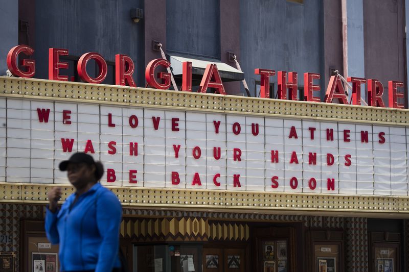 A woman walks past the Georgia Theatre Friday, March 20, 2020, in downton Athens, Ga. A note posted on the theatre's door says they are close and all shows are postponed. (AP Photo/John Bazemore)