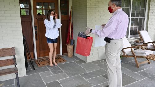 Izzy Wheeler, graduating senior, reacts as Dr. Stuart Gulley, president of Woodward Academy, personally delivers a special gift bag and yard sign at her home in College Park on Tuesday, April 28, 2020. The private school with campuses in College Park and Johns Creek, ended its school year that day, and teachers and staff personally delivered special treats and spirit wear to seniors’ houses. HYOSUB SHIN / HYOSUB.SHIN@AJC.COM