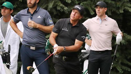 Dustin Johnson (left) and Rory McIIroy (right) look on as Phil Mickelson tees off on the 14th hole during their practice round for the Masters.