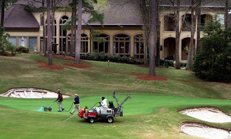 Grounds crews work on a green as a huge homes sits nearby on the golf course at the Country Club of the South in Johns Creek. AJC FILE PHOTO
